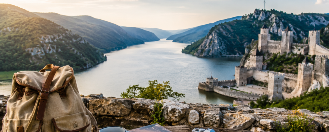 Pogled na Golubačku tvrđavu i Dunav sa rancem, mapom i fotoaparatom kao simbol vikend putovanja bez velikog budžeta.