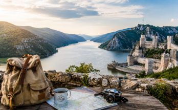 Pogled na Golubačku tvrđavu i Dunav sa rancem, mapom i fotoaparatom kao simbol vikend putovanja bez velikog budžeta.