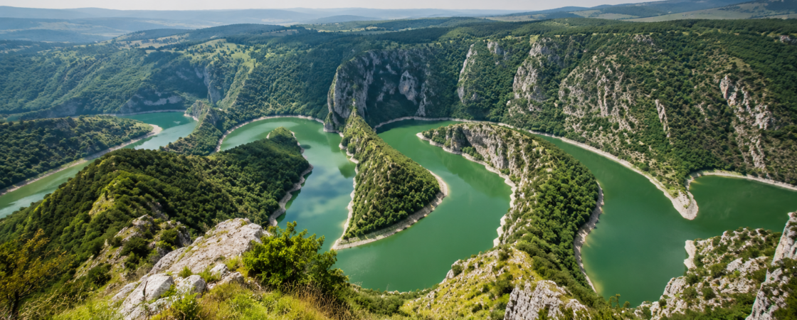 Pogled sa vidikovca na smaragdne meandre Kanjona Uvca okružene strmim krečnjačkim liticama i gustom šumom pod vedrim letnjim nebom.
