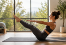 Žena izvodi pilates vežbu na prostirci u svetlom studiju sa velikim prozorima i prirodnim osvetljenjem.
